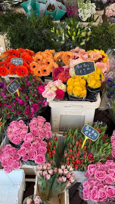 A vibrant display of fresh flowers at a flower market, showcasing various floral arrangements and bouquets. In the foreground, there are clusters of pink roses with tightly packed petals, alongside bu