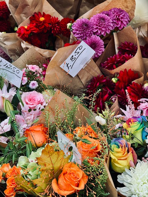 A vibrant collection of freshly cut flowers arranged in various brown paper bouquets at a flower stall. The display includes bright red, pink, purple, orange, and multicolored roses, dahlias, and chry
