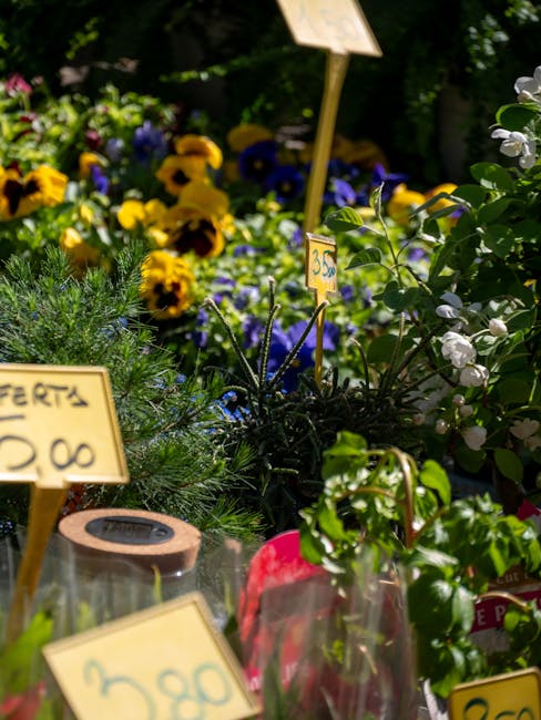 A vibrant floral display featuring a variety of fresh flowers including bright yellow pansies, purple violets, and white blossoms with dark green foliage, arranged in a natural, informal style. The fl